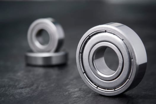 Product shot of a single ball bearing sharply pictured in the foreground with two other ball bearings positioned on top of each other in the background on a slate