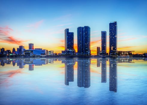 Miami city skyline panorama at dusk with urban skyscrapers over sea with reflection