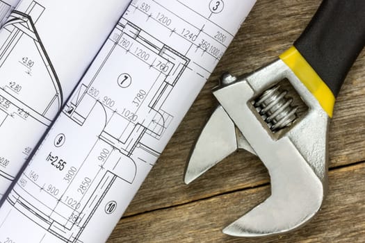 Twisted technical drawing and adjustable wrench on the wood background