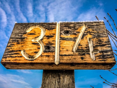A wooden plaque with the digits three and four on a pflog in the background a blue sky.