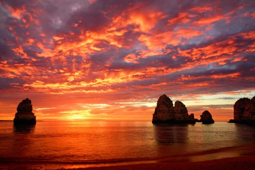 Sunrise with intense colors by the sea,with rocks and red clouds