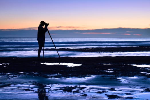 The silhouette of a man photographed with a tripod at dusk by the sea