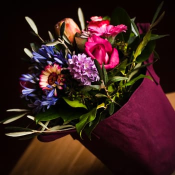 Vase like a shopping bag filled with spring flowers and with dark background - square image