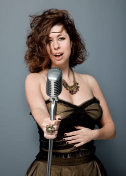 Front view studio photo of attractive young adult singer with microphone on gray background.