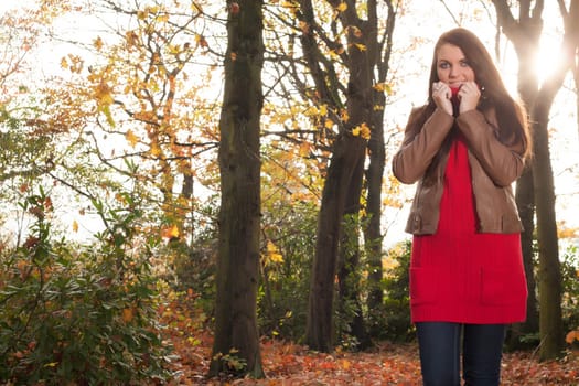 Happy brunette is having a nice time in the park while it's autumn