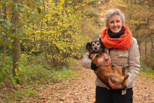 Middle aged woman in the autumn forest with her dog