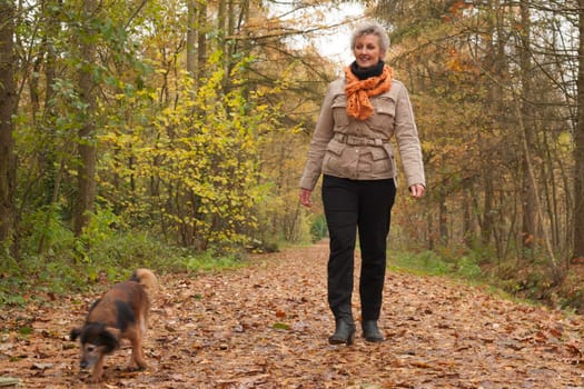 Middle aged woman in the autumn forest with her dog