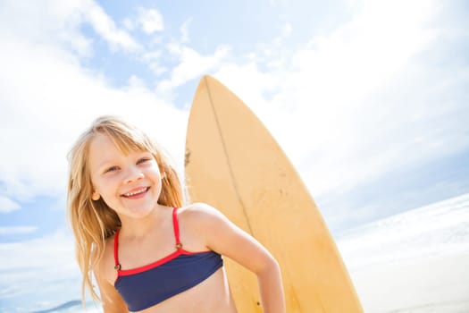 Portrait of happy smiling cute young girl with surfboard on beach with sunny sky background
