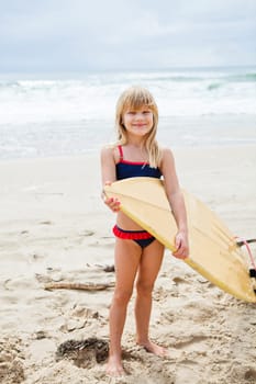 Happy smiling cute young girl holding surfboard on beach with ocean in background