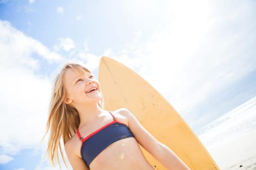 Portrait of happy smiling cute young girl with surfboard on beach with sunny sky background