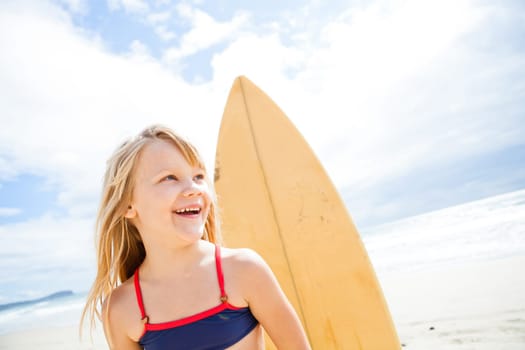 Portrait of happy smiling cute young girl with surfboard on beach with sky and ocean background
