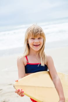 Happy smiling cute young girl with surfboard on beach with ocean in background