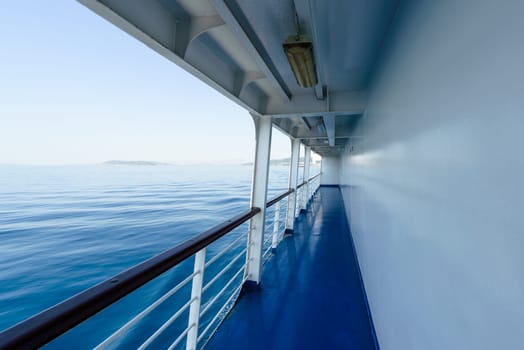 fragment of a ship deck or passenger ferry with visible railing and blue sea,in background cloudless summer sky.