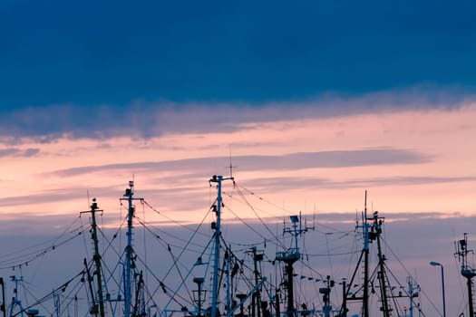 plenty of masts of fishing boats and sailing boats in sunset background,visible ropes,rigging,radars and navigation aerials,space fot text.