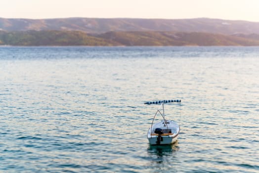 summer photo of single boat in sea,in background visible mountains and island coast,illeminated set to sun light,tilt and shift efects.
