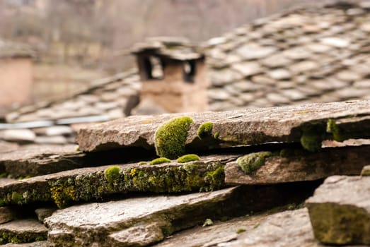 Old stone tiles and chimney of slate-roof house with fresh moss closeup