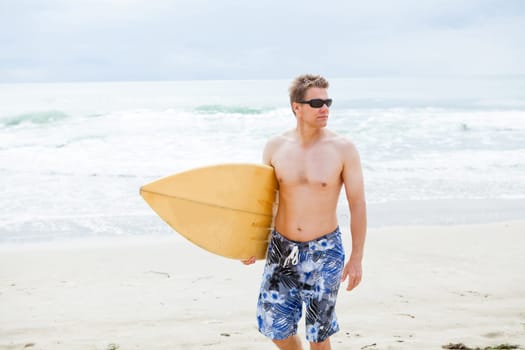 Serious looking male surfer walking on beach while carrying surfboard
