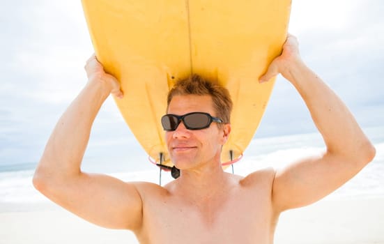 Smiling male surfer resting surfboard on head at beach with ocean and sky in background