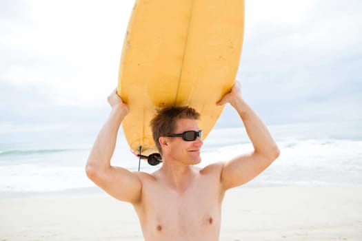 Smiling male surfer resting surfboard on head at beach with ocean and sky in background