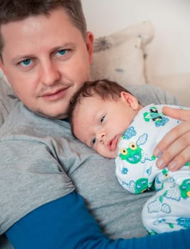 Portrait of 1 month old baby boy in his daddy's arms, almost asleep at home.