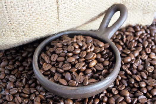 Coffee beans in a small clay pot. Image has a background of jute fibers