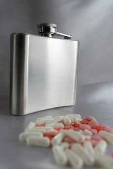 Silver metal flask with pills on a grey background.