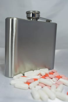 Silver metal flask with pills on a grey background.