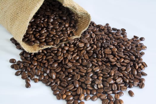 Jute bag and scattered coffee beans on a white background