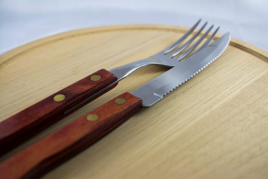 Fork and knife with red wooden handle on a plate of natural wood.