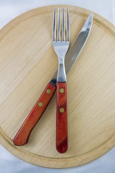 Fork and knife with red wooden handle on a plate of natural wood.