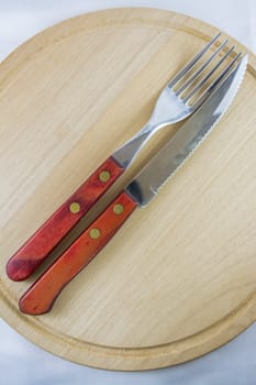 Fork and knife with red wooden handle on a plate of natural wood.