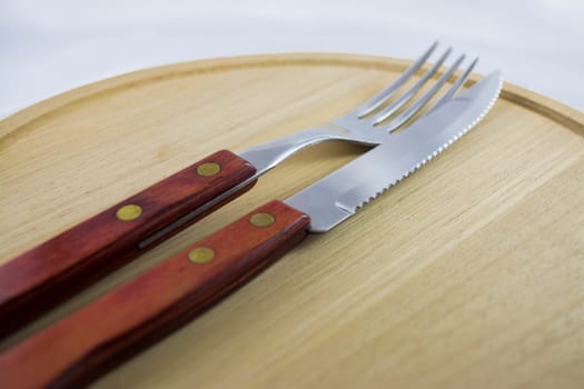 Fork and knife with red wooden handle on a plate of natural wood.