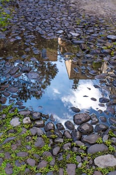 Reflections of buildings and blue sky over puddle after rain