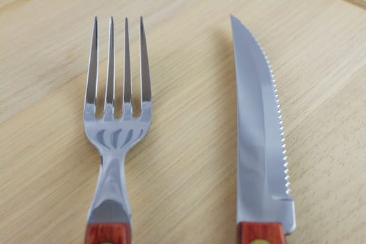 Fork and knife with red wooden handle on a plate of natural wood.