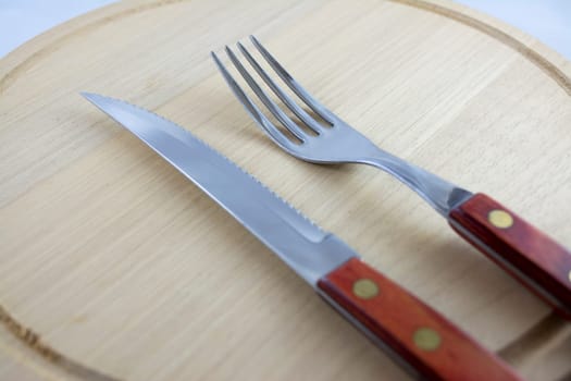 Fork and knife with red wooden handle on a plate of natural wood.