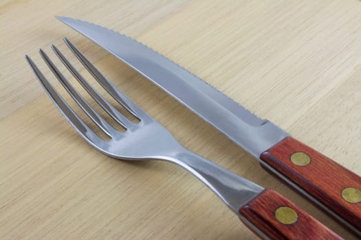 Fork and knife with red wooden handle on a plate of natural wood.