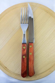 Fork and knife with red wooden handle on a plate of natural wood.