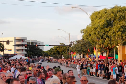 WILTON MANORS, FLORIDA - JUNE 22, 2013: Many people waiting for the LGBT pride parade on the sides of colorfully decorated with rainbow flags Wilton Drive in the evening just before a golden sunset.