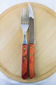 Fork and knife with red wooden handle on a plate of natural wood.