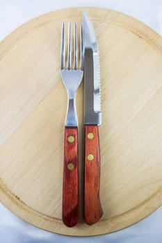 Fork and knife with red wooden handle on a plate of natural wood.