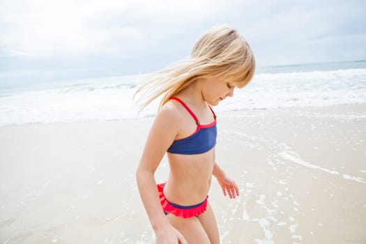 Happy cute young girl standing in water at beach on sunny day