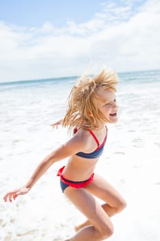Smiling cute young girl jumping and having fun at beach on sunny day