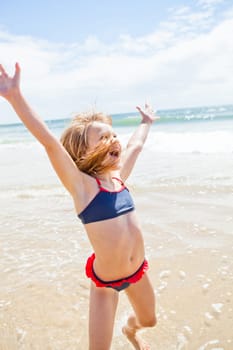 Smiling cute young girl jumping and having fun at beach on sunny day