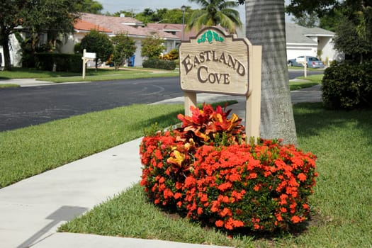 OAKLAND PARK, FLORIDA - JULY 1, 2013: Painted wood sign with orange red flowers in front of it marking the entrance to the suburban Eastland Cove neighborhood south of Prospect Road near NW 19th.