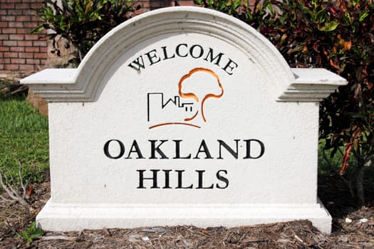 OAKLAND PARK, FLORIDA - JULY 1, 2013:  Painted cement Oakland Hills Welcome sign with graphic seen closeup outside on a sunny day with tropical foliage and a brick wall behind it.