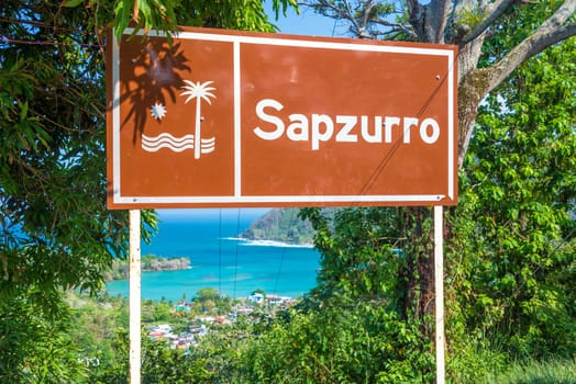 Sign at the entrance to Sapzurro with the town and bay visible below near Capurgana, Colombia