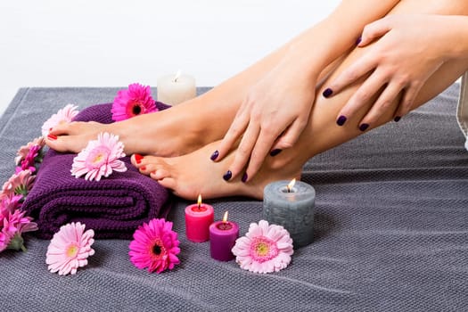 beautiful well-groomed female feet with red nail polish and flowers on towel close up wellness pedicure salon
