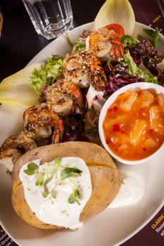 Roasted shrimp on a skewer on a mixed salad with dipp and foil potato on a plate