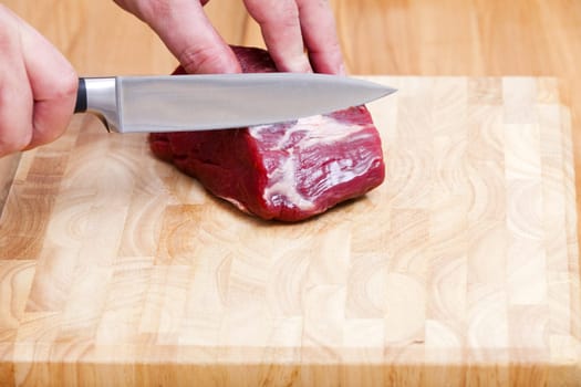 Piece of raw beef fillet is processed with a knife