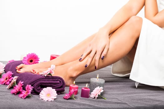 beautiful well-groomed female feet with red nail polish and flowers on towel close up wellness pedicure salon